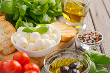 Italian food ingredients – mozzarella, tomatoes, basil and olive oil on rustic wooden background, selective focus