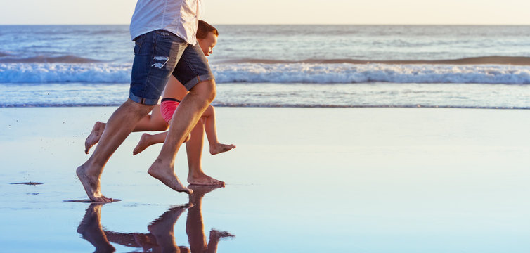 Barefoot Legs In Action. Happy Family Fun - Parents With Baby Son Running Along Edge Of Sea Beach Surf With Sunset Light. Active Travel Lifestyle, Water Activity And Game On Summer Vacation With Child