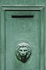 Slit of green metal mailbox with lion's head ornament 