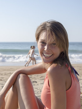 happy pretty woman smiling in the beach wearing a pink top with the sea and horizon in the background, with unrecognizable people
