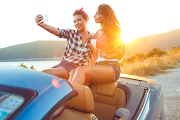 Two young beautiful girls are doing selfie in a convertible