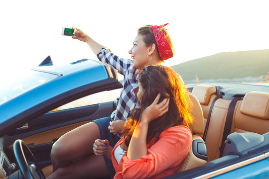 Two young beautiful girls are doing selfie in a convertible