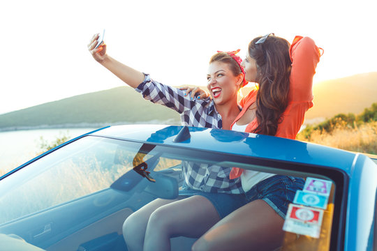 Two young beautiful girls are doing selfie in a convertible