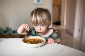 Adorable caucasian  toddler boy eating healthy soup in the kitch
