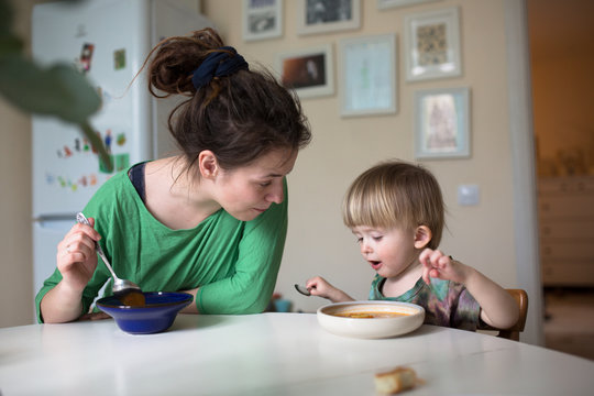 Mother With Her Baby Eating Soup In The Bright Kitchen At Home