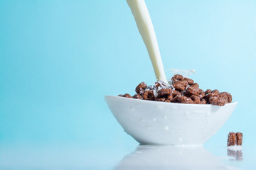 Milk stream jet pouring into a bowl with chocolate flakes in the form of rings, splashes of milk on...