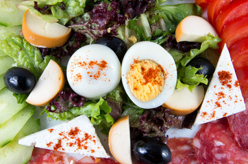 Salad with vegetables, egg, cheese and sausage.