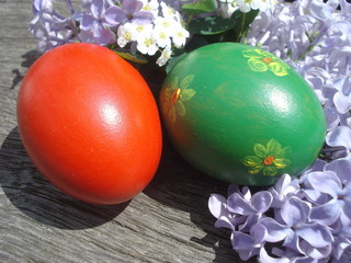 Hand painted red and green Easter eggs near lilac and spiraea flowers on wooden board