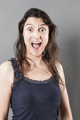 surprise concept - stunned young woman with long fine hair, mouth and eyes wide opened expressing amazement, grey background studio