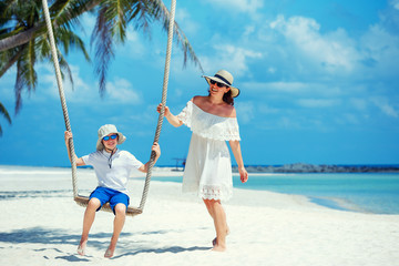 Young beautiful woman swinging son on a tropical beach, Koh Phangan island. Thailand.