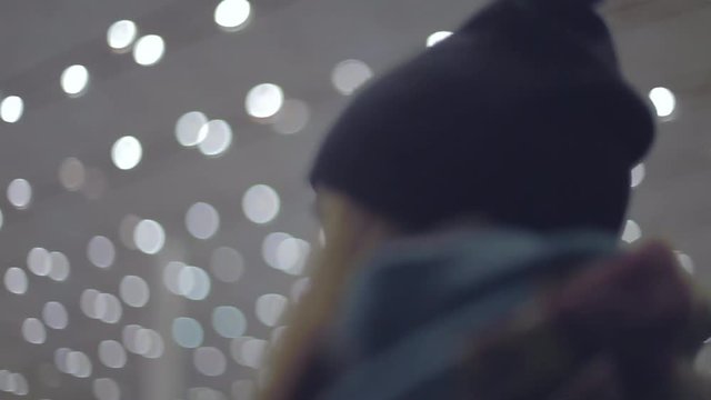 Young girl in a scarf and beanie got lost in the airport or other big building. Handheld tracking shot.