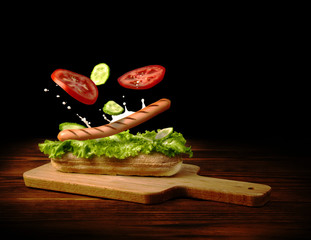 Grilled sausage with fresh vegetables falls on crispy bun, hotdog concept.
