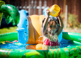 Baby girl splashing in pool with a bucket of water