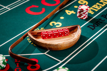 Full set of 5 dice in a wooden bowl next to the stick on a craps table with stacks of casino chip around