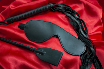 Riding crop, a whip flogger and blindfold mask on red satin, kinky sex toys for dom / sub sexual games and other forms of kink