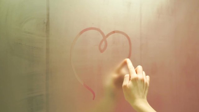 Hand draws a heart on a foggy mirror