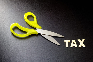 Cut tax concept. Scissors and tax alphabet on black background.