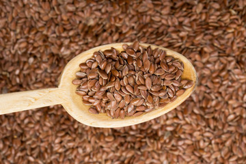 Wooden spoon with linseed coming from left seen from above over a linseed background
