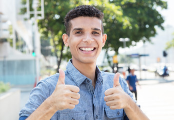Latino mit kurzen Haaren in der Stadt zeigt beide Daumen