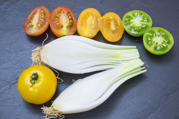 red tomatoes, yellows, greens and spring onions on a board slate
