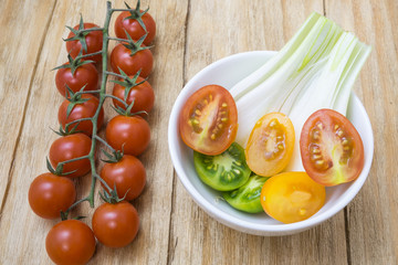 red tomatoes, yellows, greens and spring onions in a bowl on a wooden table
