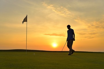 Young man playing golf at sunset
