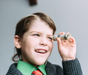 boy businessman looks through small tube from dollar