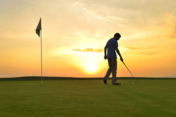 Young man playing golf at sunset