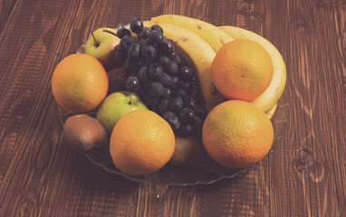 Oranges, apples, bananas and grapes are in dish