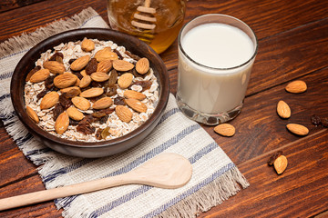 Healthy breakfast. Granola with nuts and  banana in a wooden bowl, honey and  milk  on a rustic background