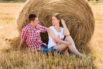 Naklejka na ściany i meble young man and woman posing in a field near a bale of hay