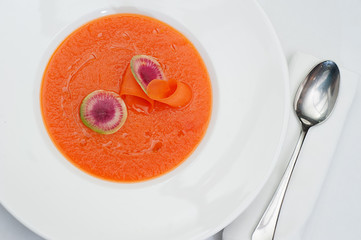 Closeup of Pumpkin Soup with Slices of Water Melon Radish in a White Plate Served on a restaurant table