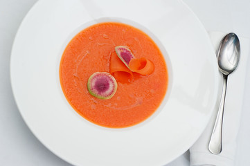 Closeup of Pumpkin Soup with Slices of Water Melon Radish in a White Plate Served on a restaurant table