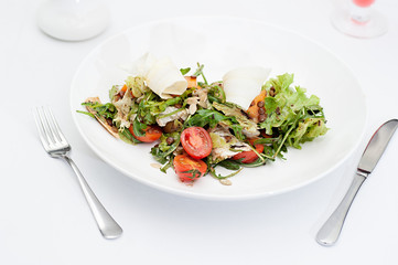 Parsnip Salad with sliced tomatoes served on a white plate in a restaurant, with fork and knife and a glass of fruit drink