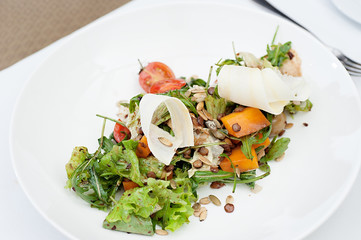 Parsnip Salad with sliced tomatoes served on a white plate in a restaurant, with fork and knife