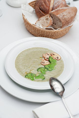 Mushrooms Cream Soup with Broccoli and Mushrooms slices served with freshly baked bread in a basket, on a restaurant table
