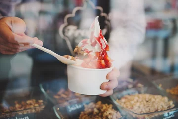 Gordijnen seller pours sauce on a soft frozen yogurt in white take away cup © very_ulissa