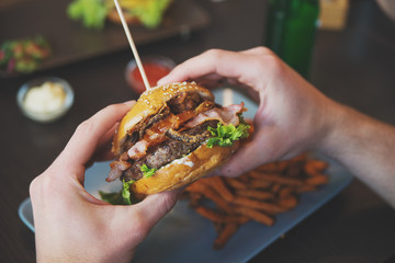 man holds burger with hands and sweet potato fries  and dips on
