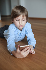 boy lying on the wooden floor and using mobile phone 