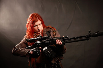 Studio shot of attractive redhead punk girl with rifle and sniper equipment, taken againstwall...