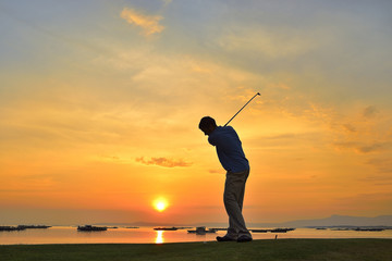Young man playing golf at sunset