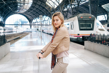 young attractive woman with blond hair waiting for the train on railway platform. modern businesswoman goes on a business trip by train