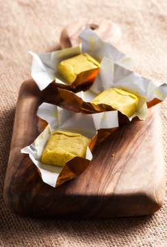 Dehydrated condiment bouillon stock cube salty meat and vegetables aromatic yellow spice, ingredient single whole portion wrapped and open in paper pack , view from above.