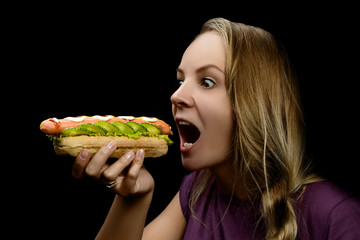 Young pretty girl eating a messy hotdog isolated on black background