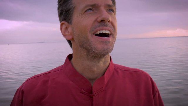 A man celebrates having it all by clentching his fists and smiling on the beach