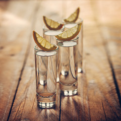 Glasses of vodka with lemon on wooden background. Toning image.