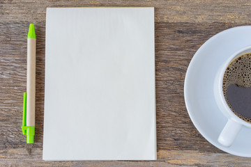 Open notebook on wooden background with coffee cup and pen.