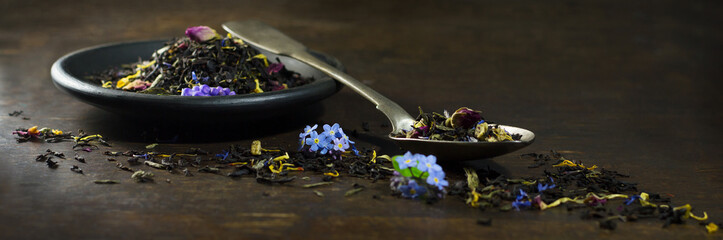 Dry tea  in spoon and plate on wooden background .