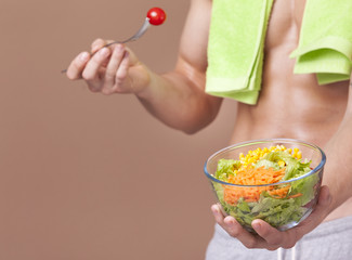 Muscled man holding a bowl of salad on brown background