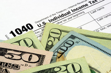 A 1040 income tax form with United States currency. The corner of the Twenty Dollar bill obscures the year to add to the image usefulness.
